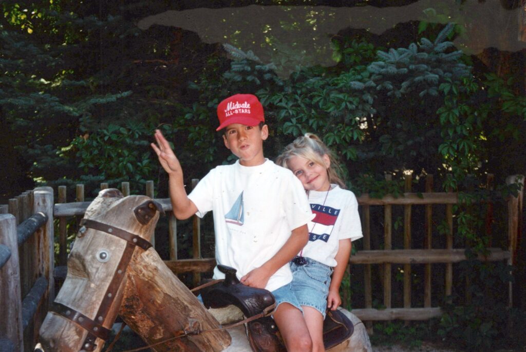 Young Vince waving from a wooden horse beside a small girl.